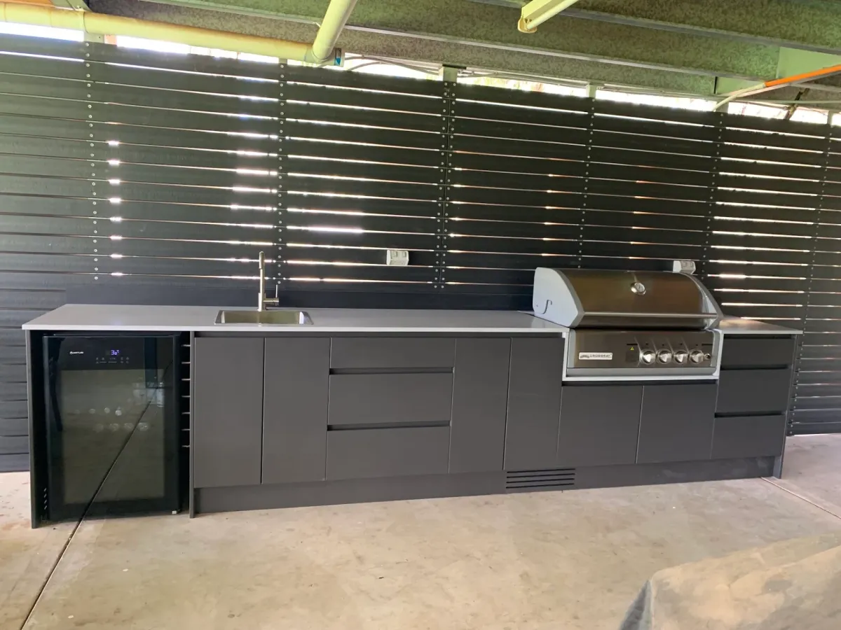 Custom outdoor kitchen with built-in sink, BBQ and glass-door wine fridge against dark slat wall