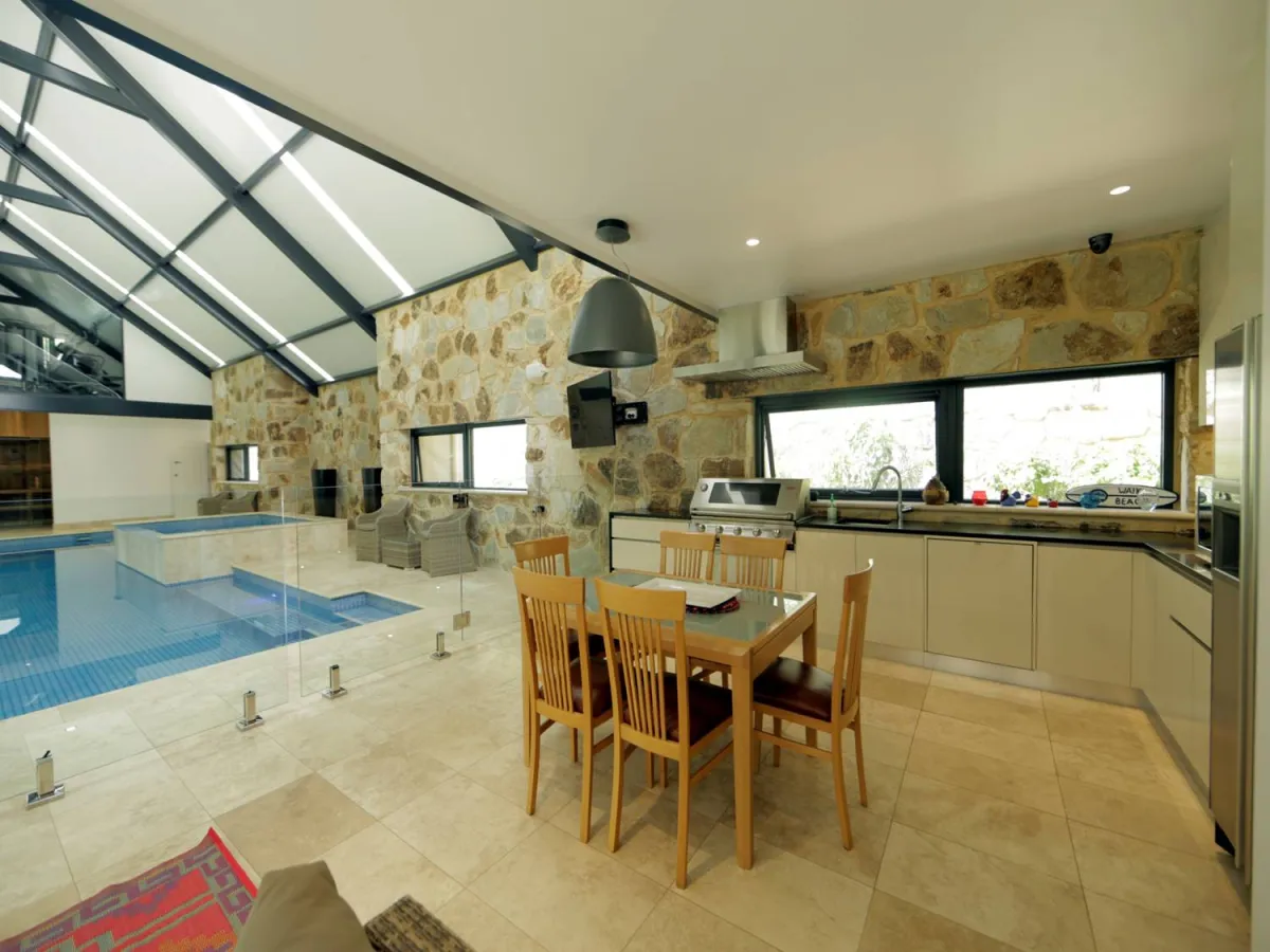 Indoor-outdoor alfresco space with stone walls, swimming pool, dining area and outdoor kitchen
